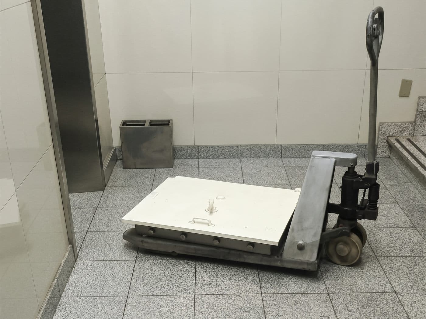 Caja fuerte recostada sobre una transpaleta en el hall de un edificio de oficinas, junto al ascensor