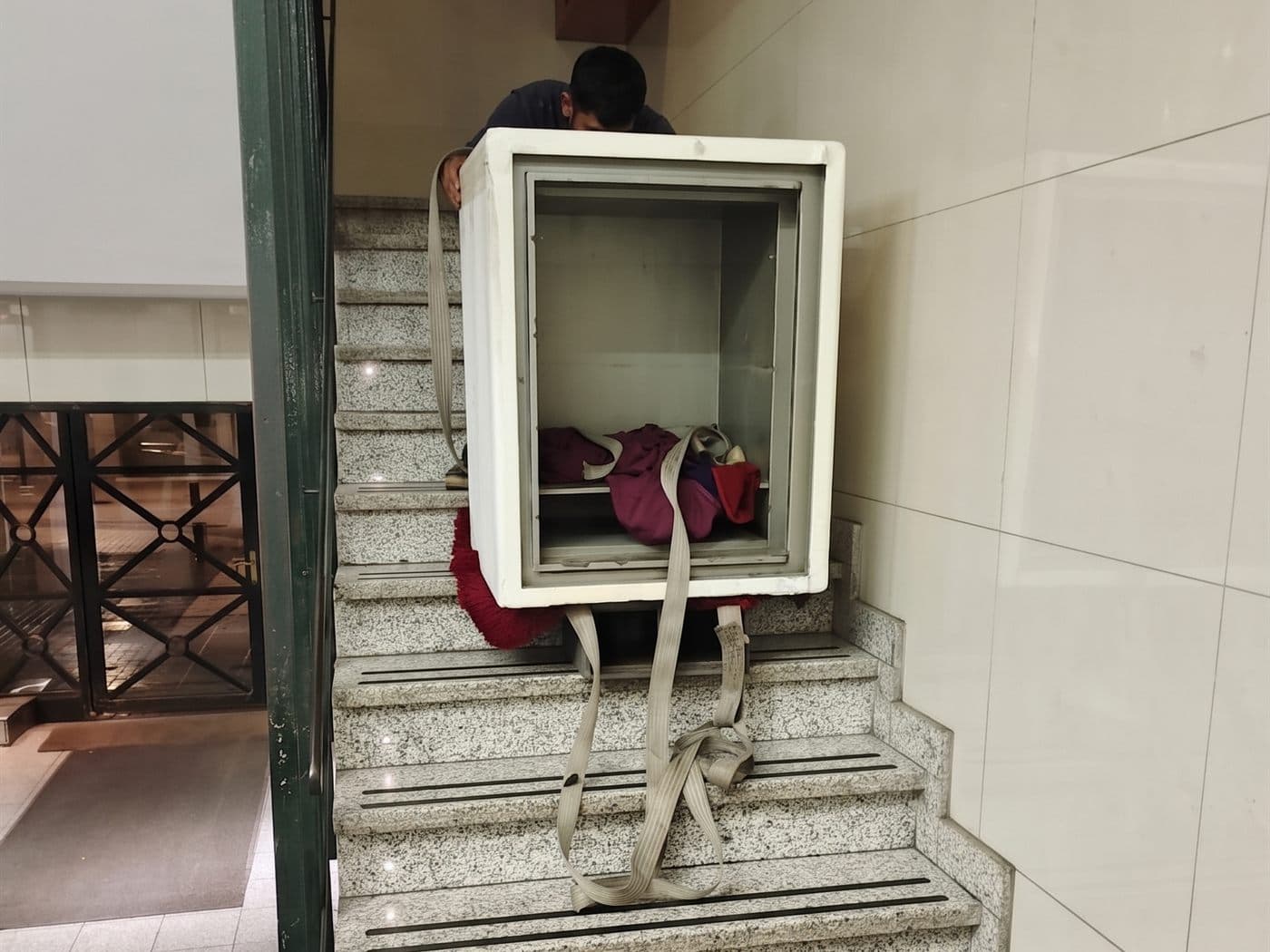 Caja fuerte sujeta con correas mientras el equipo de traslado la baja por una escalera de granito