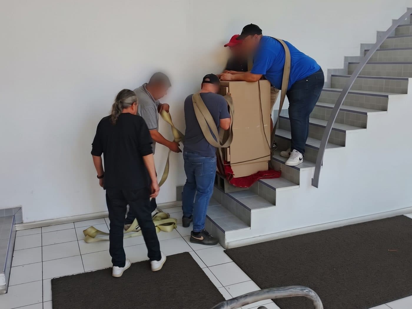 Equipo sujetando con correas una caja fuerte embalada en cartón sobre los primeros peldaños de la escalera de una oficina