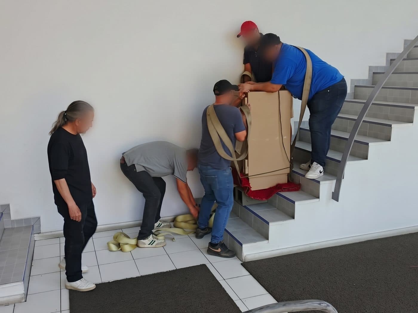 Equipo de traslado preparando las correas al pie de la escalera mientras el resto afirma la caja fuerte embalada en cartón sobre los peldaños