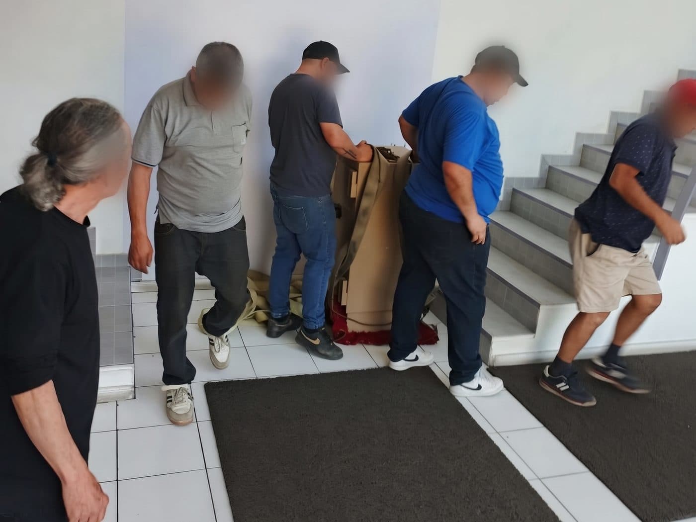 Caja fuerte embalada en cartón y amarrada con una correa al pie de la escalera de una oficina, con el equipo alrededor