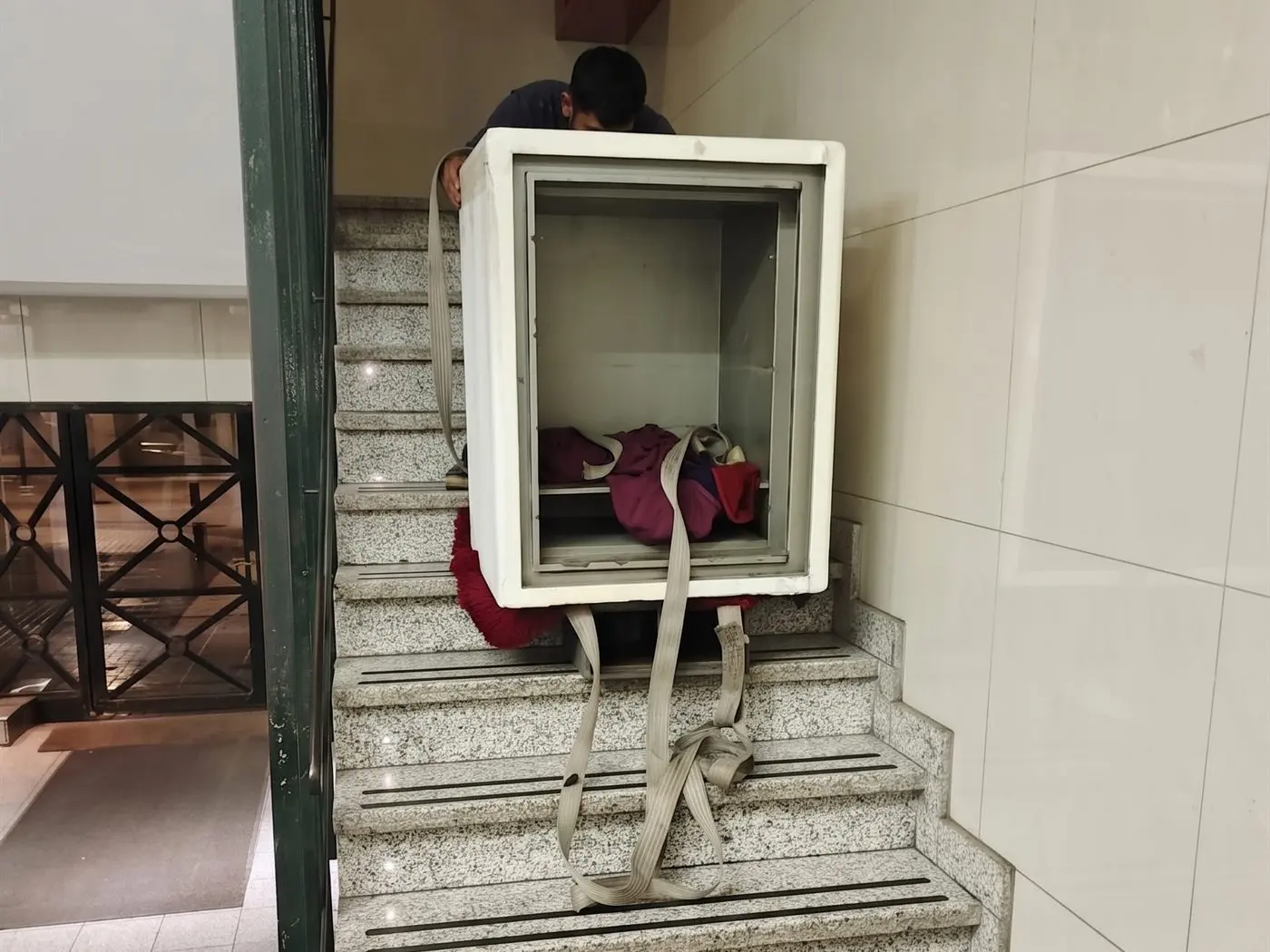 Caja fuerte sujeta con correas mientras el equipo de traslado la baja por una escalera de granito