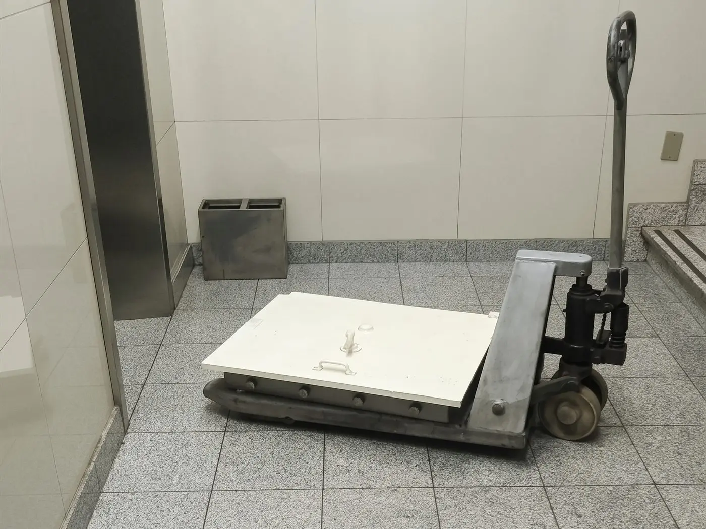 Caja fuerte recostada sobre una transpaleta en el hall de un edificio de oficinas, junto al ascensor